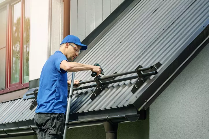 mężczyzna montujący zabezpieczenie przeciw osuwaniu się śniegu na dachu